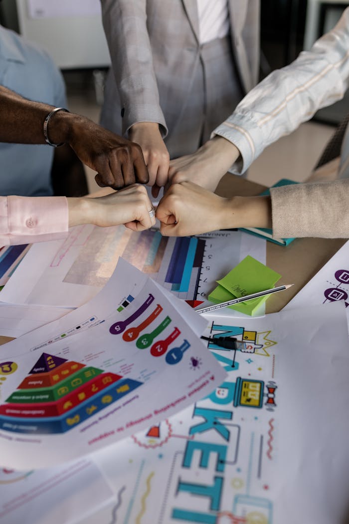 A group collaborates with a fist bump over colorful marketing charts, showcasing teamwork.