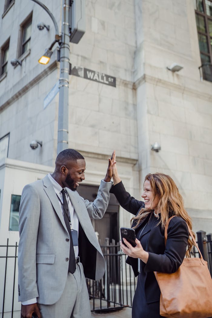 African American man and Caucasian woman sharing a high five on Wall Street, NYC.